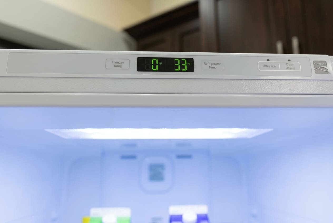 Close-up of a Kenmore refrigerator digital control panel with green LED display reading freezer temperature at 0°F and refrigerator at 38°F, featuring Ultra Ice and Door Alarm buttons.